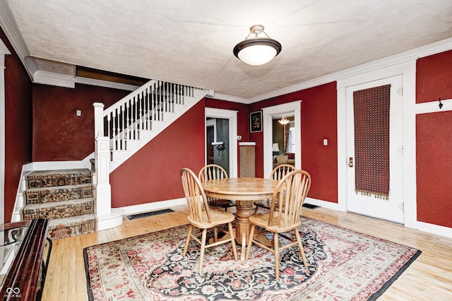 dining area featuring hardwood / wood-style flooring, crown molding, and a textured ceiling