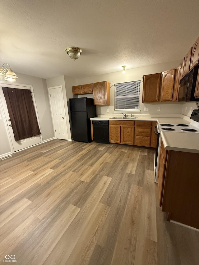 kitchen featuring sink, black appliances, a textured ceiling, and light wood-type flooring