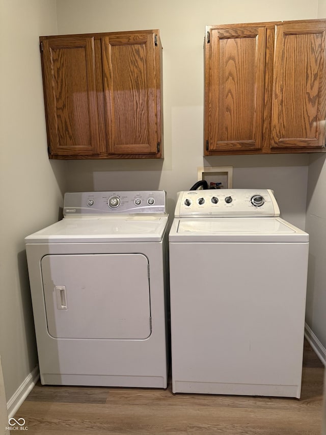 clothes washing area featuring washer and clothes dryer, cabinets, and light wood-type flooring