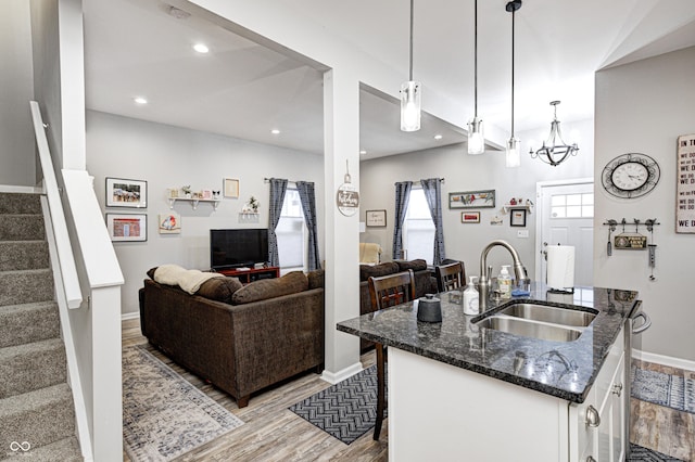 kitchen featuring a kitchen bar, sink, hanging light fixtures, dark stone countertops, and an island with sink
