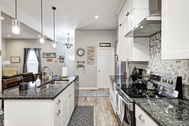 kitchen with wall chimney exhaust hood, sink, a center island with sink, dark stone countertops, and stainless steel appliances