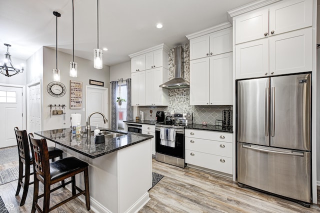 kitchen featuring sink, stainless steel appliances, an island with sink, white cabinets, and wall chimney exhaust hood