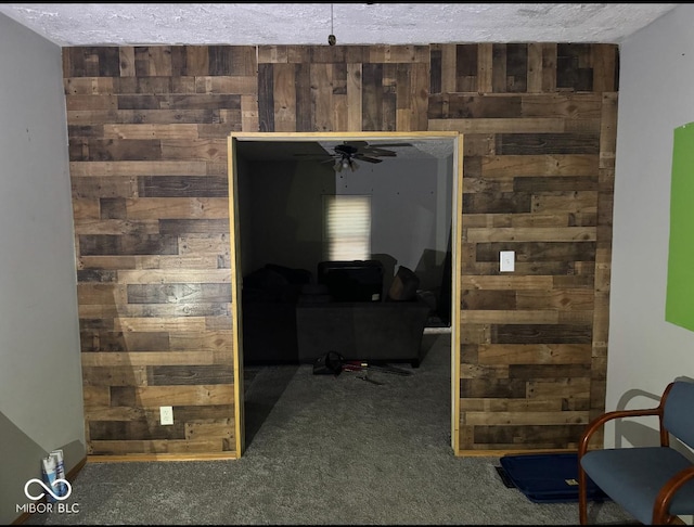 interior space with wooden walls, a textured ceiling, and dark colored carpet