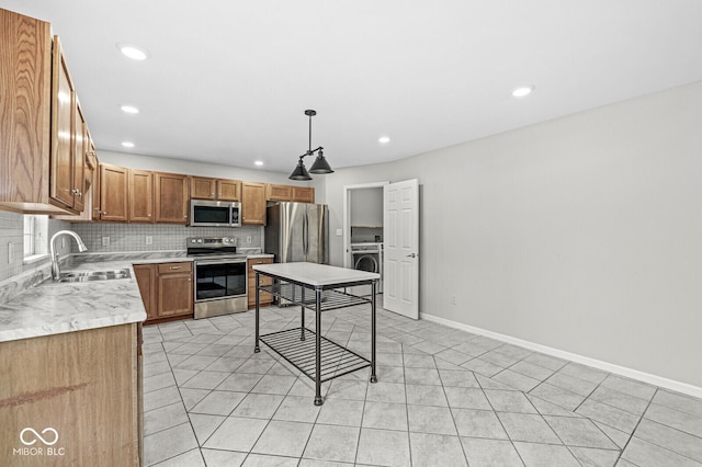 kitchen with appliances with stainless steel finishes, decorative light fixtures, washer / clothes dryer, tasteful backsplash, and sink