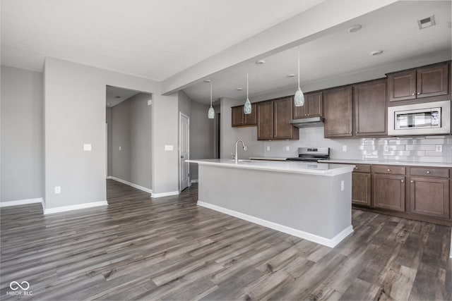 kitchen featuring pendant lighting, appliances with stainless steel finishes, dark brown cabinetry, a center island with sink, and decorative backsplash