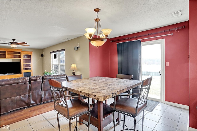 tiled dining room featuring ceiling fan with notable chandelier, a textured ceiling, and a wealth of natural light