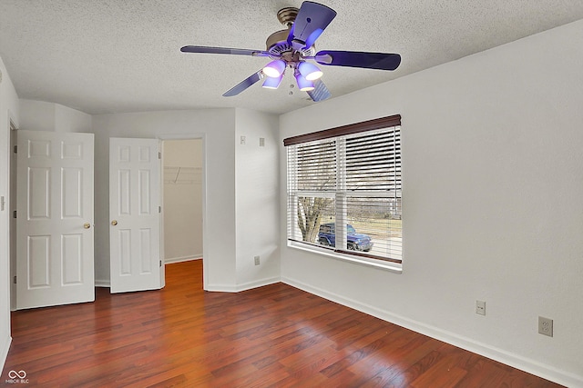 unfurnished bedroom featuring dark hardwood / wood-style floors, a spacious closet, ceiling fan, a textured ceiling, and a closet