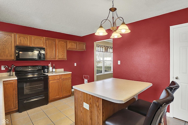 kitchen with light tile patterned flooring, hanging light fixtures, a center island, black appliances, and a textured ceiling