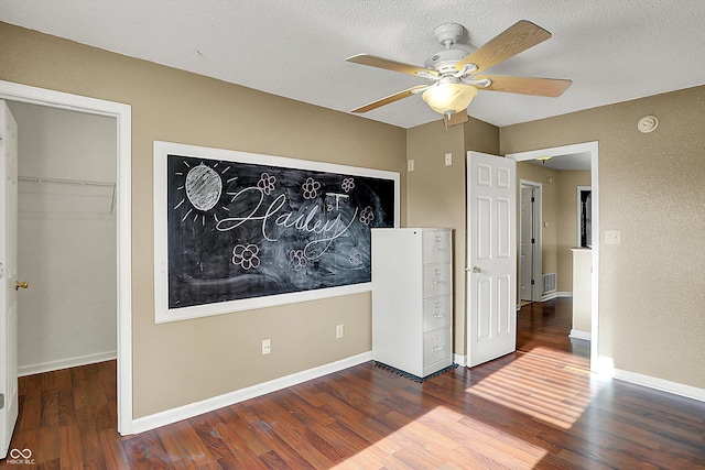 unfurnished bedroom featuring a closet, dark wood-type flooring, a textured ceiling, and a spacious closet