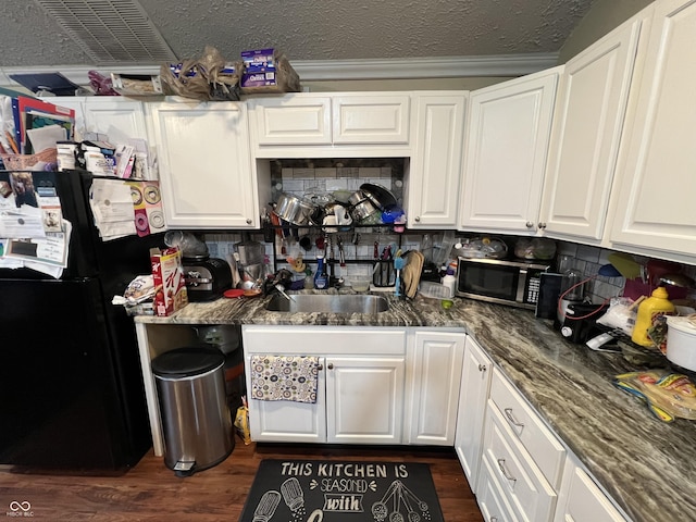 kitchen with black fridge, dark stone counters, dark wood-type flooring, and white cabinets