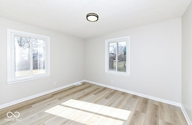 spare room featuring light wood-type flooring, visible vents, baseboards, and a wealth of natural light