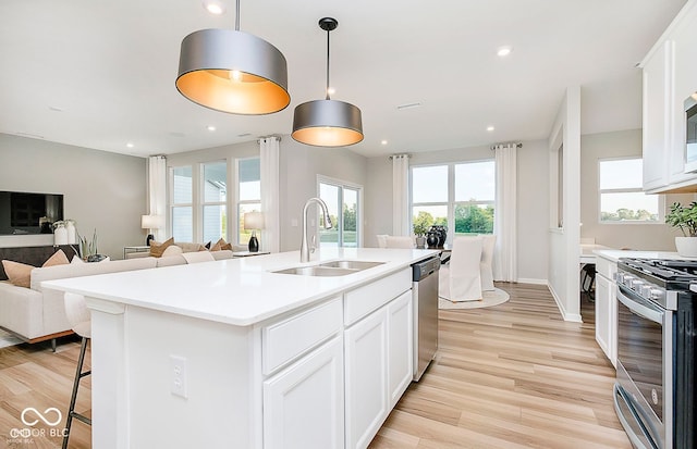 kitchen featuring pendant lighting, white cabinetry, stainless steel appliances, and a center island with sink