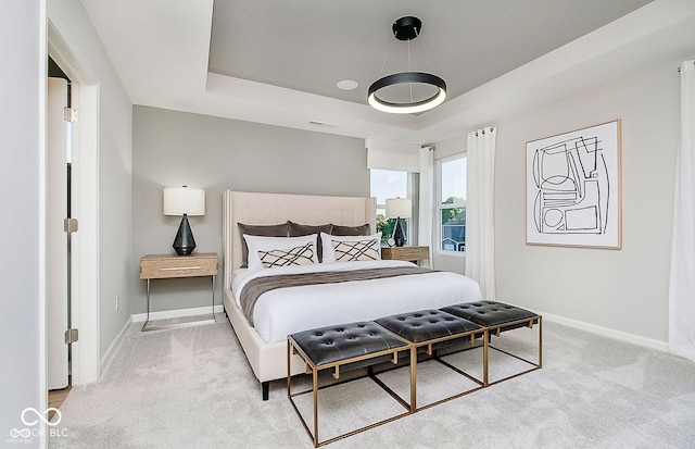 bedroom featuring light carpet, a raised ceiling, and baseboards