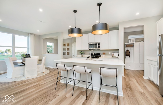 kitchen featuring stainless steel appliances, white cabinetry, a center island with sink, and decorative light fixtures