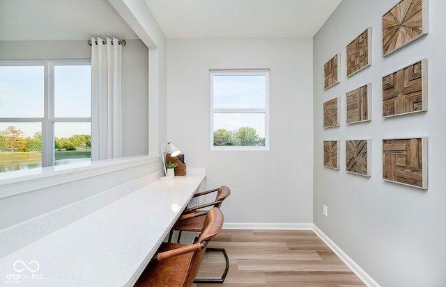 home office with a water view, plenty of natural light, baseboards, and light wood-style flooring