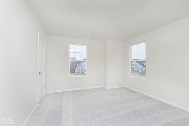 spare room featuring light colored carpet, plenty of natural light, visible vents, and baseboards