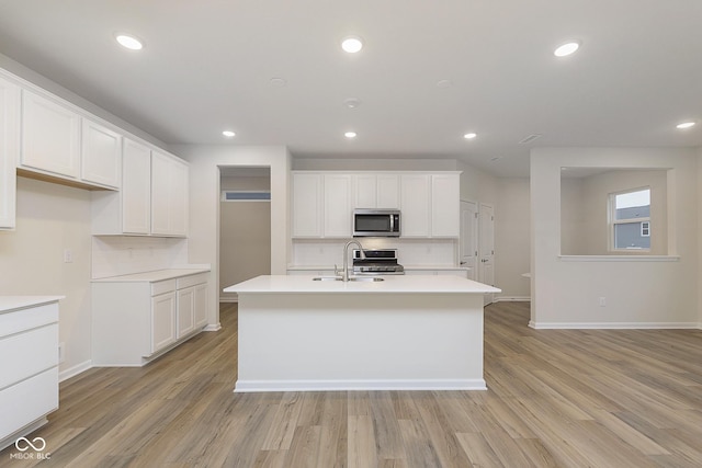 kitchen featuring stainless steel appliances, white cabinets, light countertops, and a center island with sink