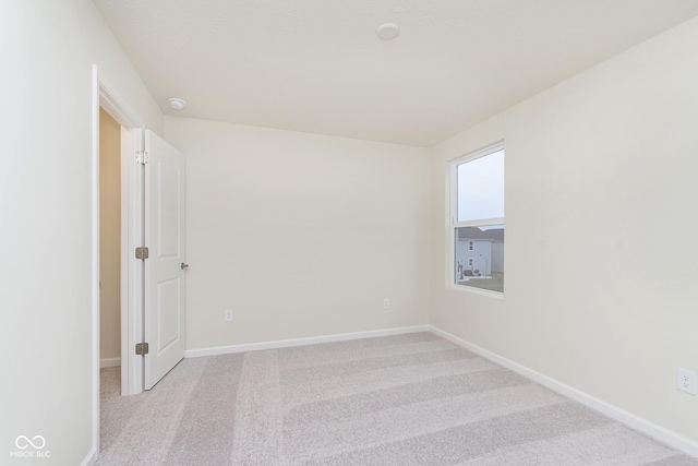 spare room featuring light carpet and baseboards