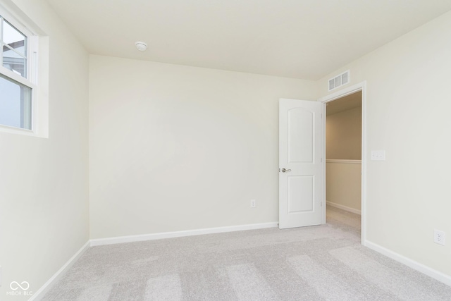 unfurnished room featuring light colored carpet, visible vents, and baseboards