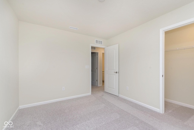 unfurnished bedroom with a walk in closet, a closet, light colored carpet, visible vents, and baseboards