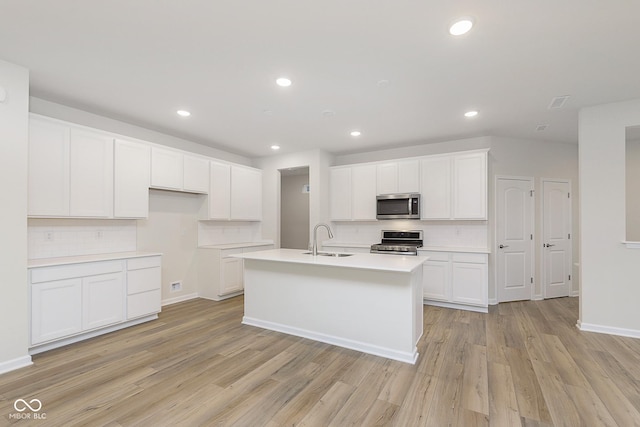 kitchen featuring a kitchen island with sink, a sink, white cabinets, light countertops, and appliances with stainless steel finishes