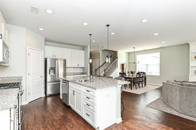 kitchen featuring an island with sink, white cabinetry, stainless steel appliances, and hanging light fixtures