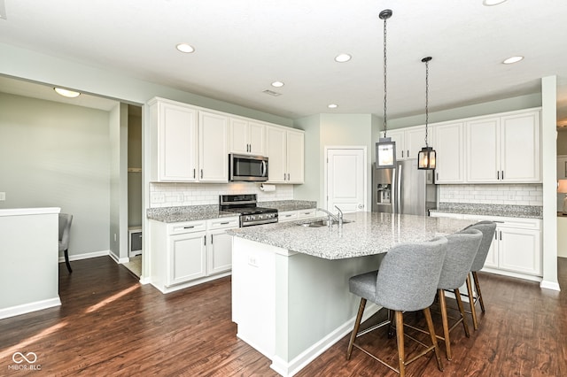 kitchen featuring stainless steel appliances, a sink, white cabinets, hanging light fixtures, and an island with sink