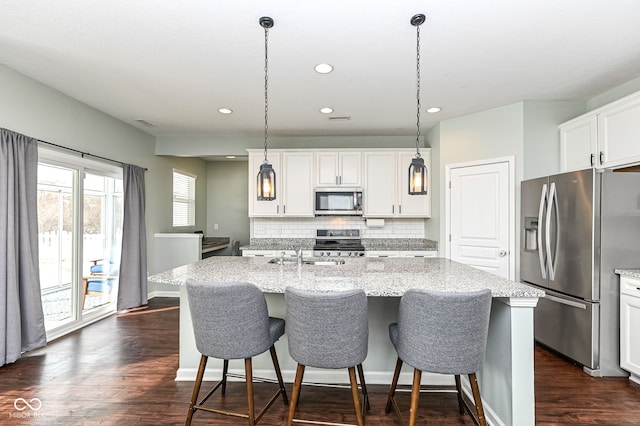 kitchen with stainless steel appliances, light stone counters, a center island with sink, and decorative light fixtures