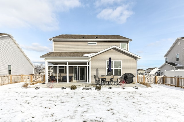 snow covered house featuring a fenced backyard and a sunroom