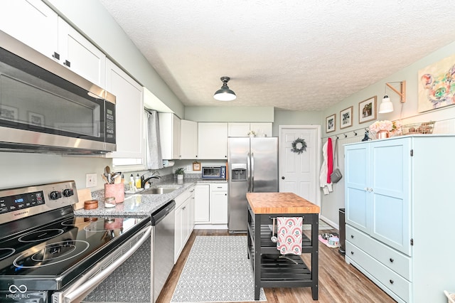 kitchen with stainless steel appliances, butcher block counters, a sink, white cabinets, and light wood finished floors