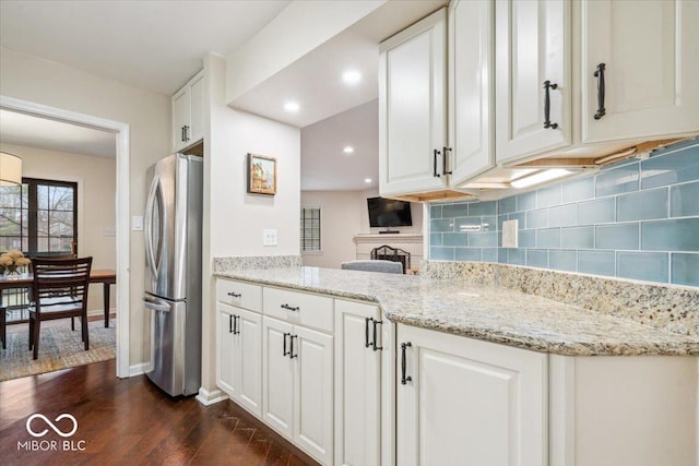 kitchen with dark wood-type flooring, stainless steel refrigerator, light stone countertops, white cabinets, and decorative backsplash