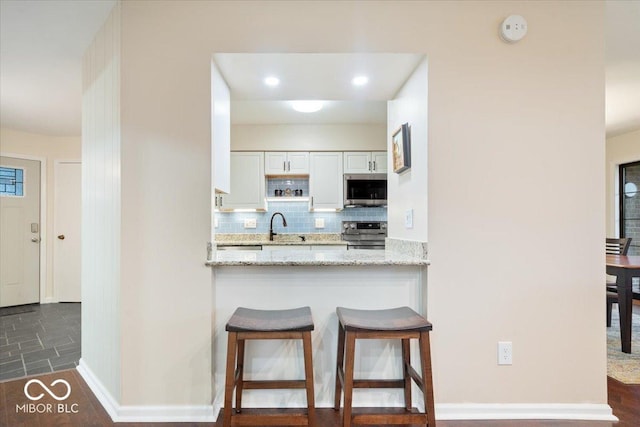 kitchen featuring white cabinetry, stainless steel appliances, light stone countertops, a kitchen bar, and decorative backsplash