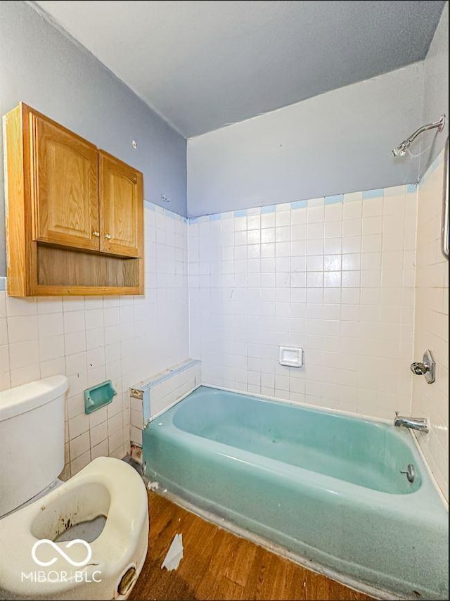 bathroom featuring wood-type flooring, shower / bathing tub combination, tile walls, and toilet