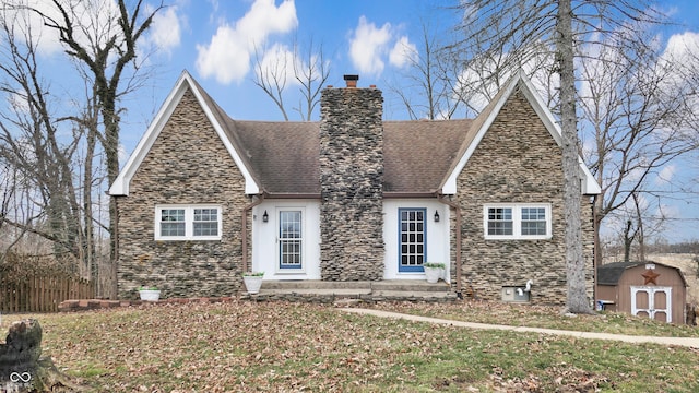 tudor house with an outbuilding, a chimney, stucco siding, a storage shed, and stone siding