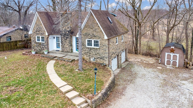 view of front facade with a storage unit, fence, a garage, stone siding, and driveway