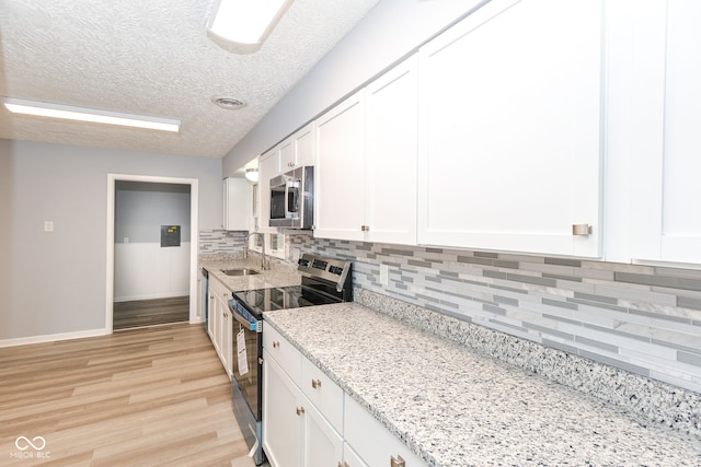 kitchen with appliances with stainless steel finishes, sink, white cabinets, light stone counters, and light wood-type flooring