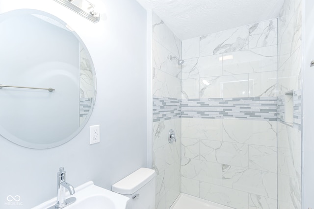 bathroom with a tile shower, sink, and toilet