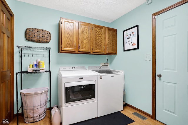 laundry room with a textured ceiling, cabinets, washing machine and clothes dryer, and light wood-type flooring