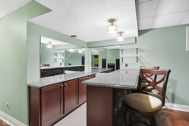 kitchen with dark brown cabinets, a kitchen breakfast bar, a center island, light stone countertops, and a textured ceiling