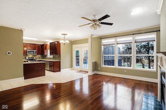 kitchen featuring appliances with stainless steel finishes, ceiling fan with notable chandelier, pendant lighting, tasteful backsplash, and light hardwood / wood-style flooring