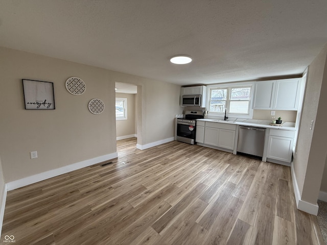 kitchen with appliances with stainless steel finishes, white cabinetry, sink, light hardwood / wood-style floors, and a textured ceiling