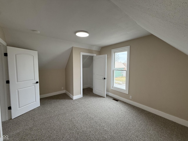 additional living space with carpet flooring, vaulted ceiling, and a textured ceiling