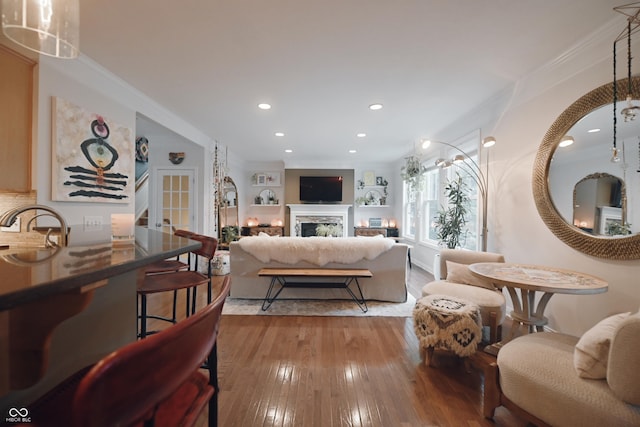 living room with sink, ornamental molding, and light wood-type flooring