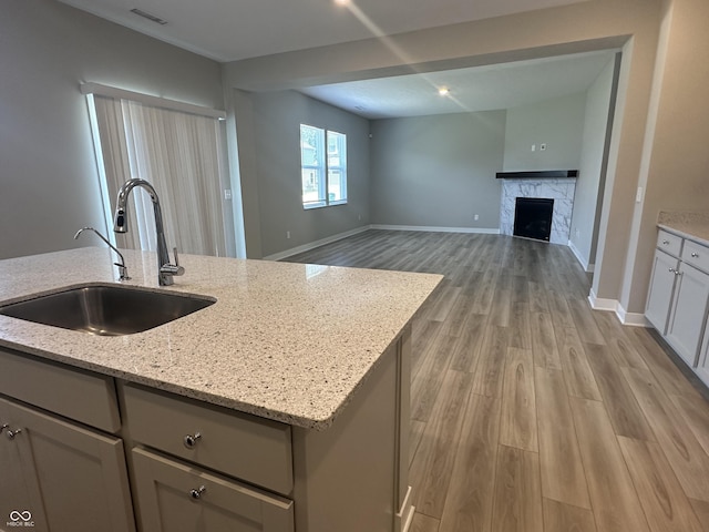 kitchen with light stone counters, light hardwood / wood-style floors, sink, and a center island with sink