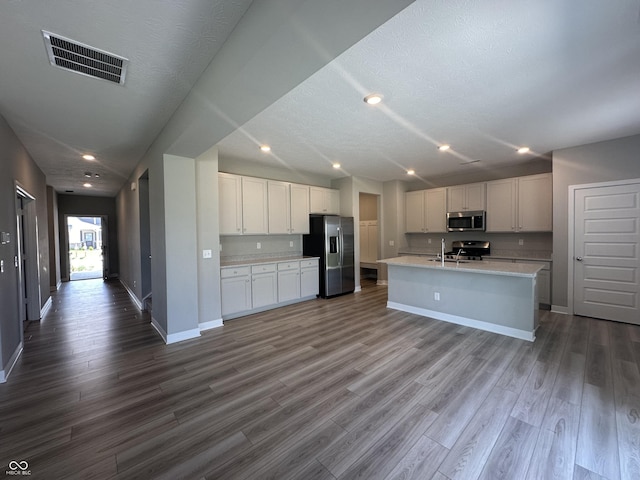 kitchen featuring white cabinetry, hardwood / wood-style floors, stainless steel appliances, and a center island with sink