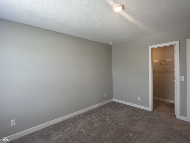 unfurnished bedroom featuring a walk in closet, dark carpet, a closet, and a textured ceiling