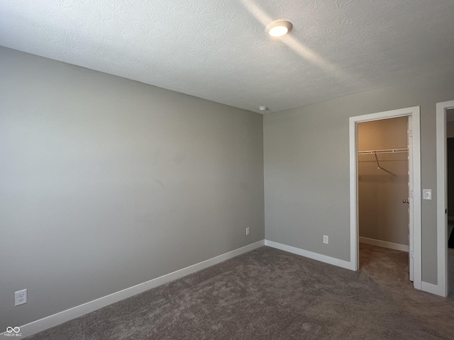 unfurnished bedroom featuring dark colored carpet, a spacious closet, a textured ceiling, and a closet