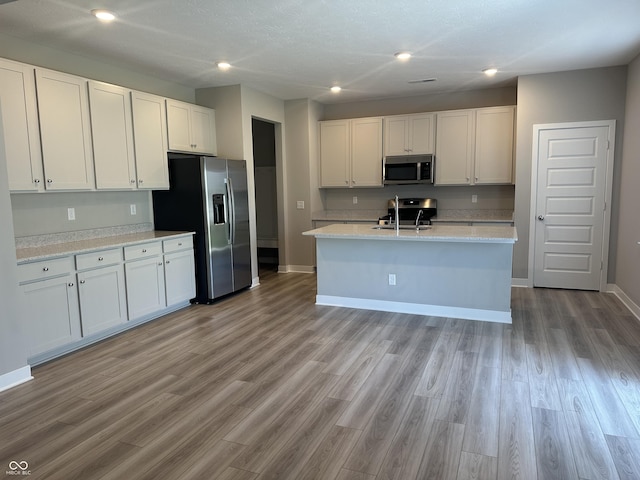 kitchen with stainless steel appliances, white cabinetry, a kitchen island with sink, and light hardwood / wood-style flooring