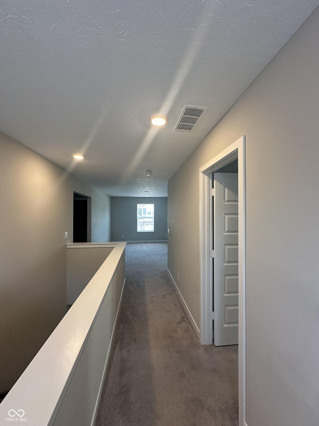 hallway featuring a textured ceiling and dark colored carpet