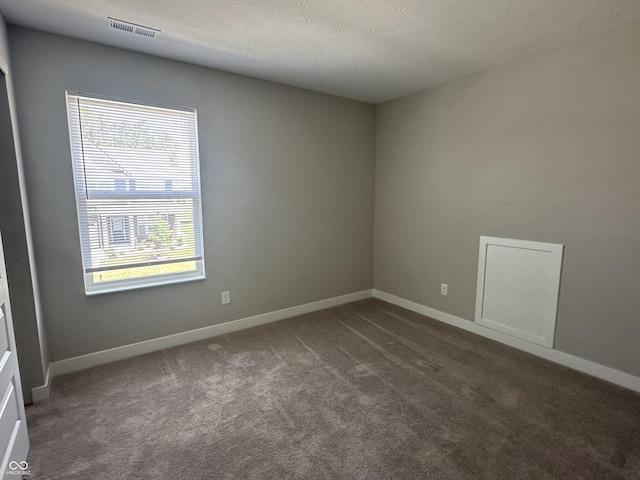 spare room featuring a textured ceiling and dark colored carpet